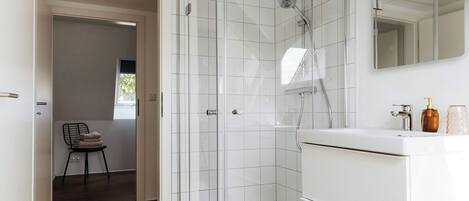 Een moderne badkamer met een douchecabine van glas, een witte wastafel en een spiegel erboven.