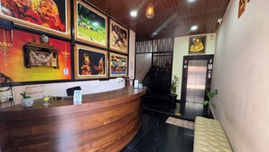 A reception desk with framed artwork, a wooden counter, and a black tiled floor. - Sri Sai Lodge Manipal (Udupi)