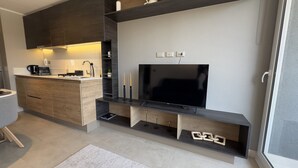 A modern kitchen with a built-in TV, wooden cabinets, and a coffee maker. - Oceana Suites Ñuñoa (Santiago)