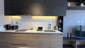 A modern kitchen with dark cabinetry, a white countertop, a built-in sink, and a stainless steel refrigerator. - Oceana Suites Ñuñoa (Santiago)
