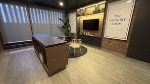 Una lavanderia moderna con una scrivania in legno, una sedia, una TV e un cartello che indica l'apertura 24 ore su 24.