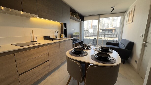 A modern kitchen with a dining area, built-in appliances, and a view of the city. - Oceana Suites Ñuñoa (Santiago)