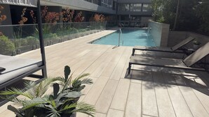 A pool area with lounge chairs, a glass railing, and potted plants. - Oceana Suites Ñuñoa (Santiago)