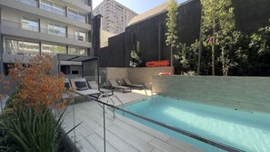 Una piscina sul tetto con lettini, ringhiera in vetro e vista su un grattacielo.