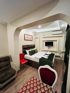 Ein Hotelzimmer mit einem Bett, einem roten Sessel, einer Couch, einem an der Wand montierten Fernseher und einem kleinen Tisch mit einer Lampe.
