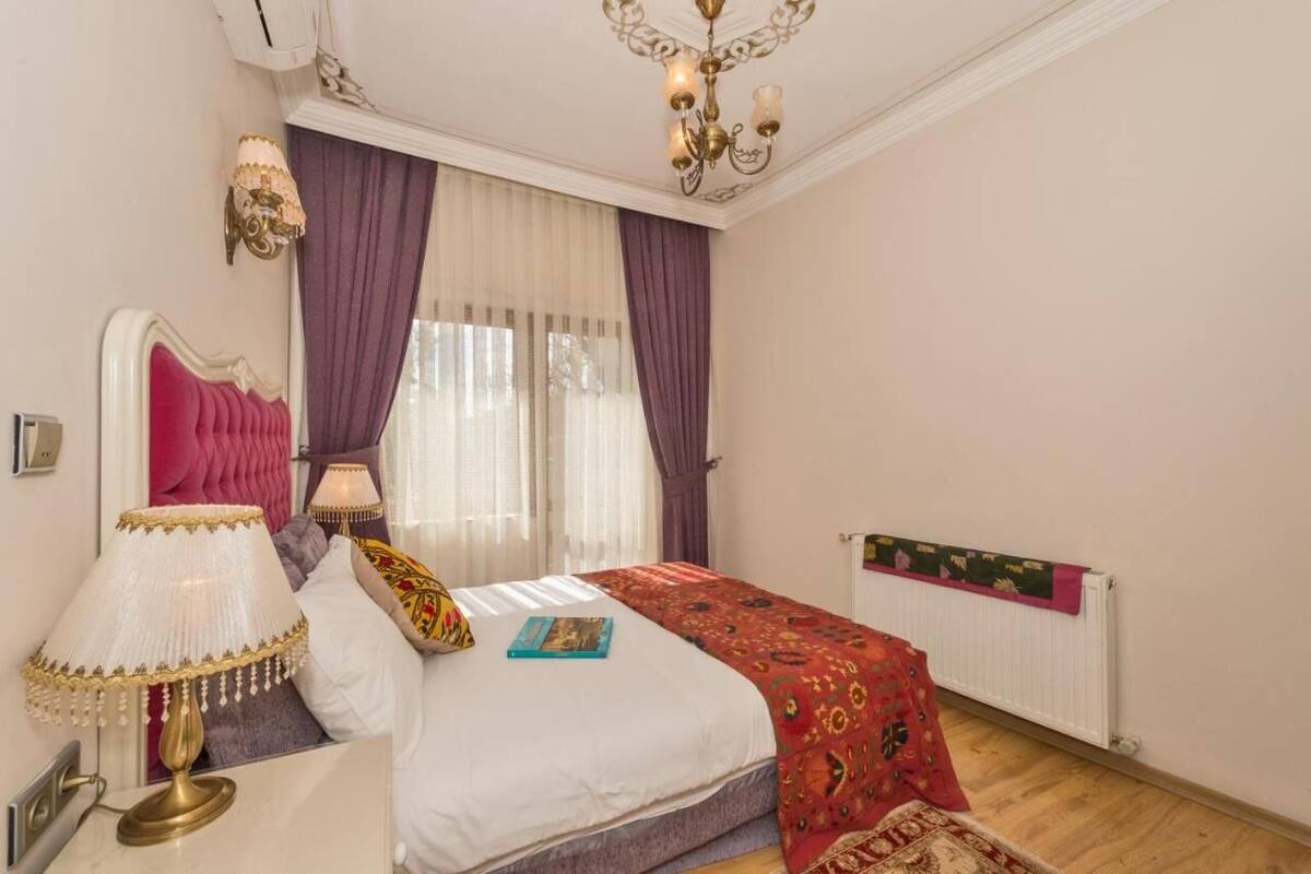 Ein Schlafzimmer mit Bett, Nachttisch, Lampe, einer Kandelaber und einem Fenster mit Vorhängen.