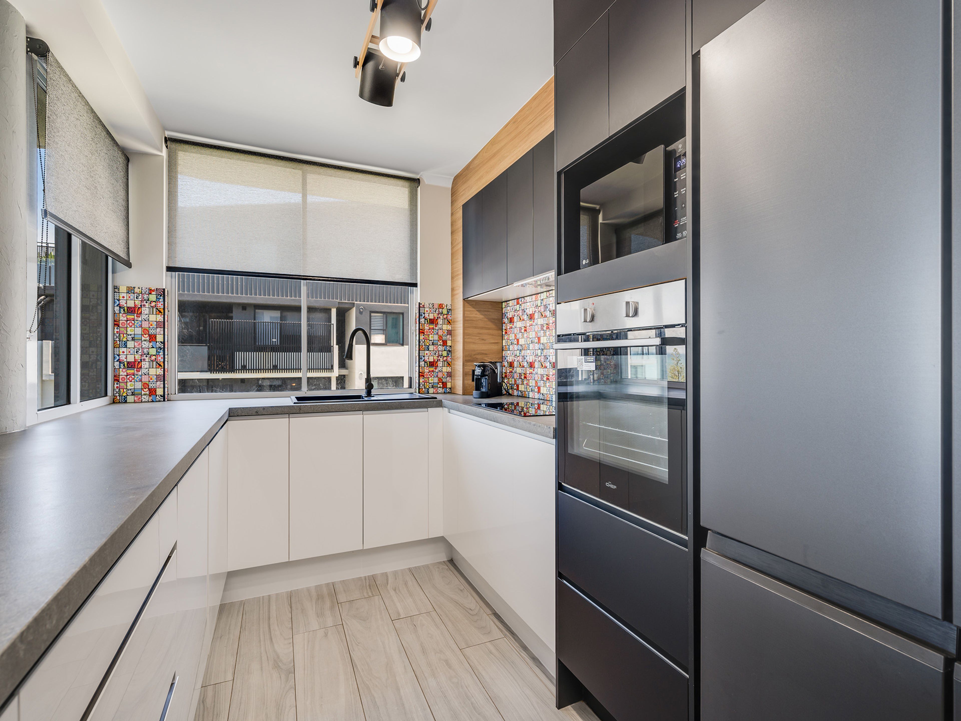 A modern kitchen with a built-in oven, a stainless steel refrigerator, and a large window with blinds.