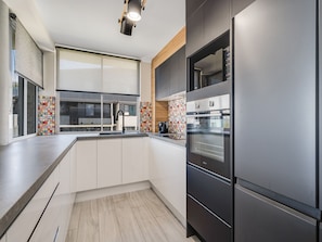 A modern kitchen with a built-in oven, a stainless steel refrigerator, and a large window with blinds. - Aurora Pacific U12 Walk To Kings Beach & Shops (Kings Beach)