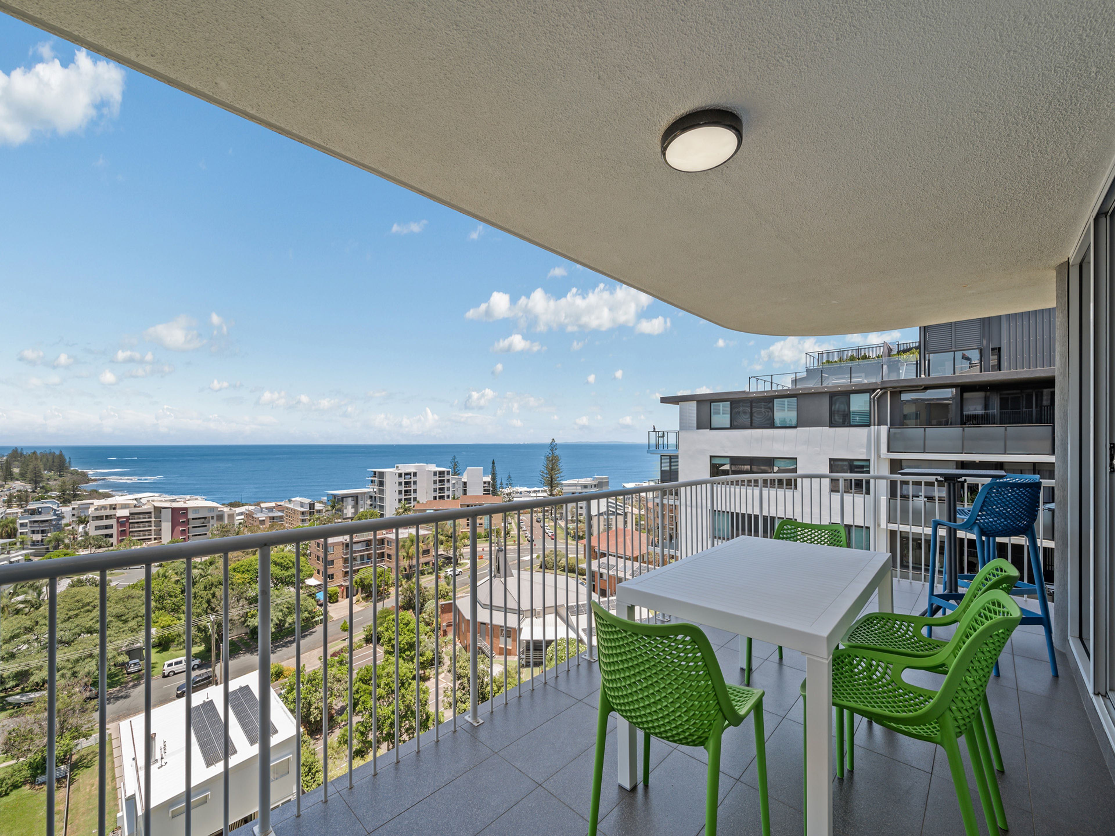 Un balcon avec une table et des chaises, offrant une vue sur la côte, avec des bâtiments et un ciel dégagé.