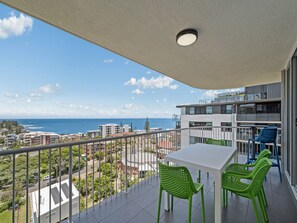 Ein Balkon mit Tisch und Stühlen, der auf eine Küstenlandschaft mit Gebäuden und einem klaren Himmel blickt.
