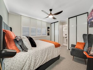 Quarto com cama, cadeira, ventoinha no teto e janela com persianas.