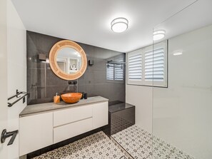 Ein modernes Badezimmer mit rundem Spiegel, einem Waschbecken aus Holz und Fliesen mit Muster.