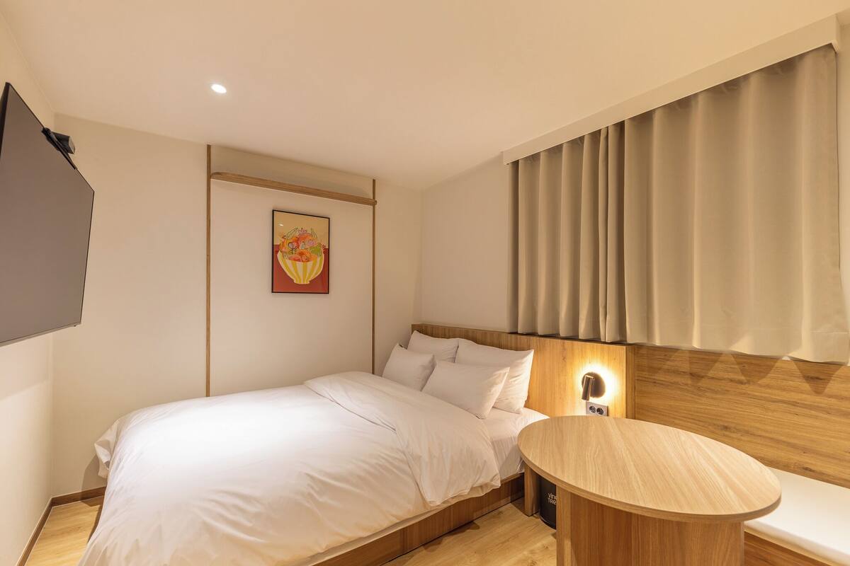 Una habitación de hotel moderna con una cama de madera, una mesa redonda de madera y una lámpara fijada a la pared.