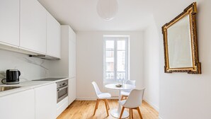 Eine moderne Küche mit weißen Schränken, einer schwarzen Kaffeemaschine und einem Essbereich mit zwei weißen Stühlen und einem runden Tisch.