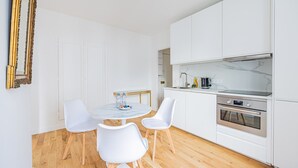 Eine moderne Küche mit weißen Schränken, einer Marmorarbeitsplatte und Edelstahlgeräten. In der Mitte befindet sich ein runder Tisch mit weißen Stühlen.