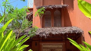 A traditional building with a thatched roof, ornate doors, and a courtyard with potted plants and wicker furniture.