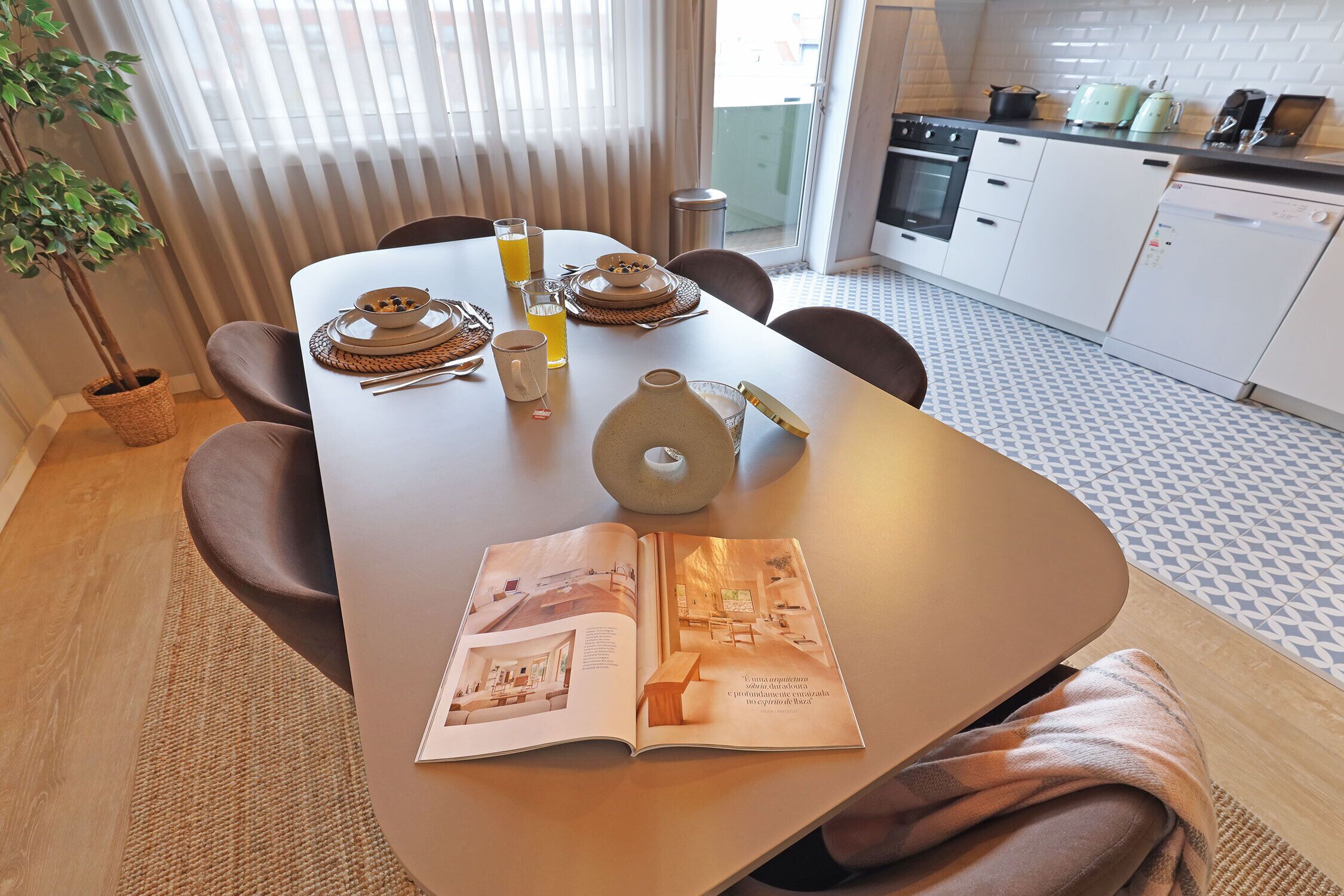 Un área de comedor con una mesa dispuesta para dos, una revista abierta y una planta en maceta.