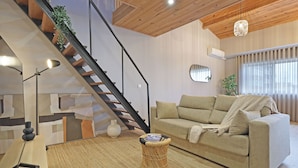 A modern living room with a sofa, a wicker stool, a staircase, and a large window. - ON Apartments - Family - Free Parking & Pet Friendly (Porto)