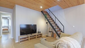 A modern living room with a flat-screen TV, wooden flooring, a staircase, and a cozy sofa. - ON Apartments - Family - Free Parking & Pet Friendly (Porto)