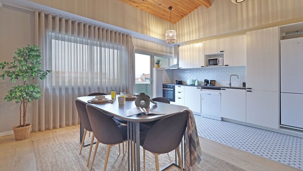A modern kitchen with white cabinets, a microwave, and a sink. There is a dining area with a table and chairs, and a potted plant. - ON Apartments - Family - Free Parking & Pet Friendly (Porto)