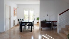 A spacious room with a dining table, chairs, a potted plant, a vintage radio, and a staircase.