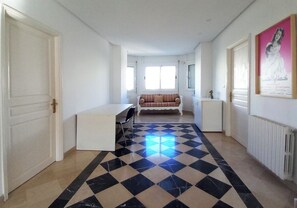 Ein geräumiges Zimmer mit Schachbrettmuster-Boden, einer Couch, einem Schreibtisch und einer Heizung.