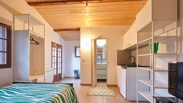 A bedroom with a bed, a wardrobe, a television, and a kitchen area. - Cosy Cabin “Cabane Grenobloise” with Shared Garden (Eybens)