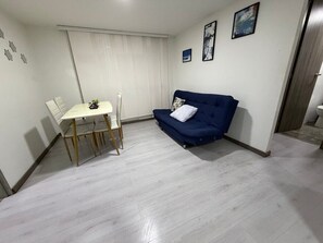 Een kamer met een eettafel en stoelen, een blauwe bank en een raam met gordijnen.