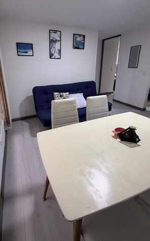 Ein Zimmer mit einem weißen Tisch, zwei Stühlen, einem blauen Sofa und drei gerahmten Kunstwerken an der Wand.