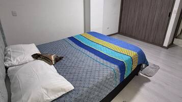 Une chambre à coucher avec un lit, des oreillers, une couverture, un plancher en bois et une armoire.