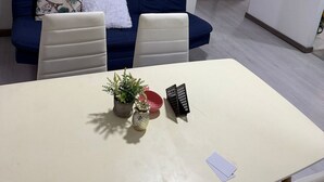 Un salon moderne avec un canapé bleu, deux fauteuils blancs, une petite table sur laquelle se trouve une plante et un bol rouge, ainsi que trois œuvres d’art encadrées accrochées au mur.