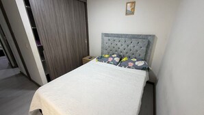 A bedroom with a bed, a nightstand, a grey headboard, and a door leading to a balcony. - Comfortable Apartment – Stratum 5 (Manizales)