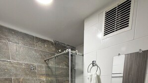 A bathroom with a glass-enclosed shower, a toilet, a sink with a mirror, and a towel rack. - Comfortable Apartment – Stratum 5 (Manizales)