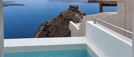 Una piscina con agua azul cristalina, un borde de piedra y vistas al mar y a islas distantes.