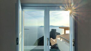 A room with a glass door leading to a balcony with a view of the sea and distant land. - DIAMOND on the cliff Hotel &Suites (Santorini)
