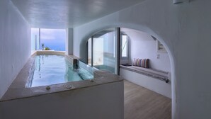 A modern interior with a pool, arched windows, and a view of the sea. - DIAMOND on the cliff Hotel &Suites (Santorini)