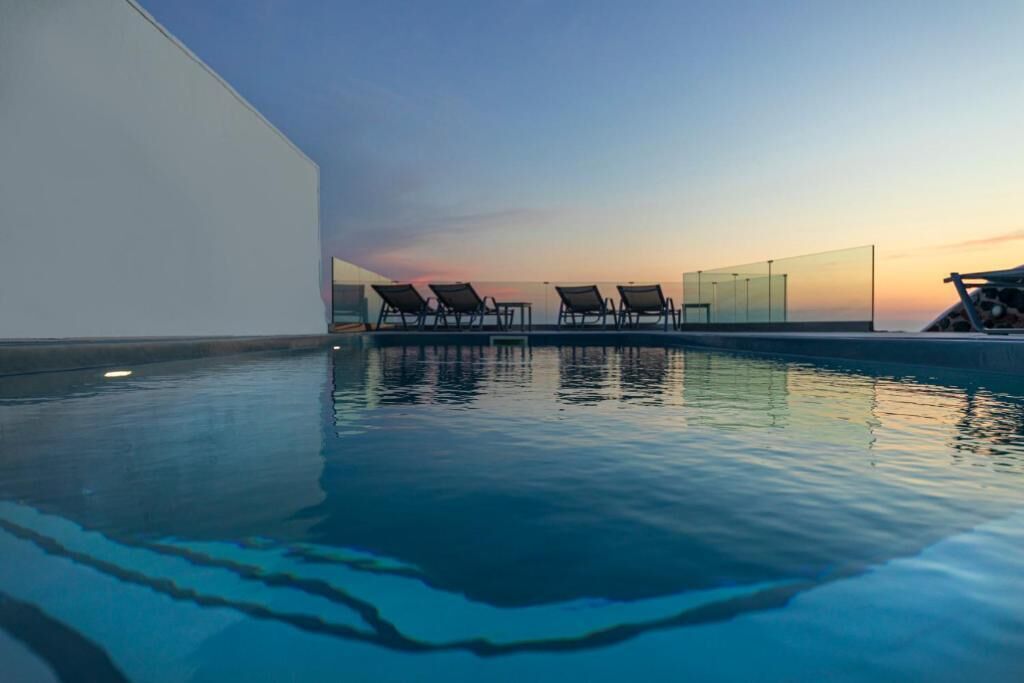 A modern pool area with clear blue water, a sunset view, and several lounge chairs.