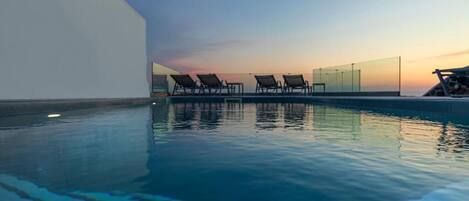 A modern pool area with clear blue water, a sunset view, and several lounge chairs.