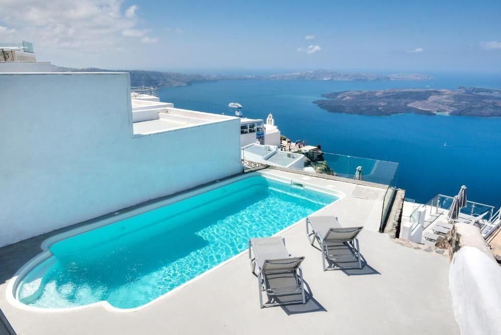 A rooftop pool with clear blue water, white walls, and a view of the sea and islands.