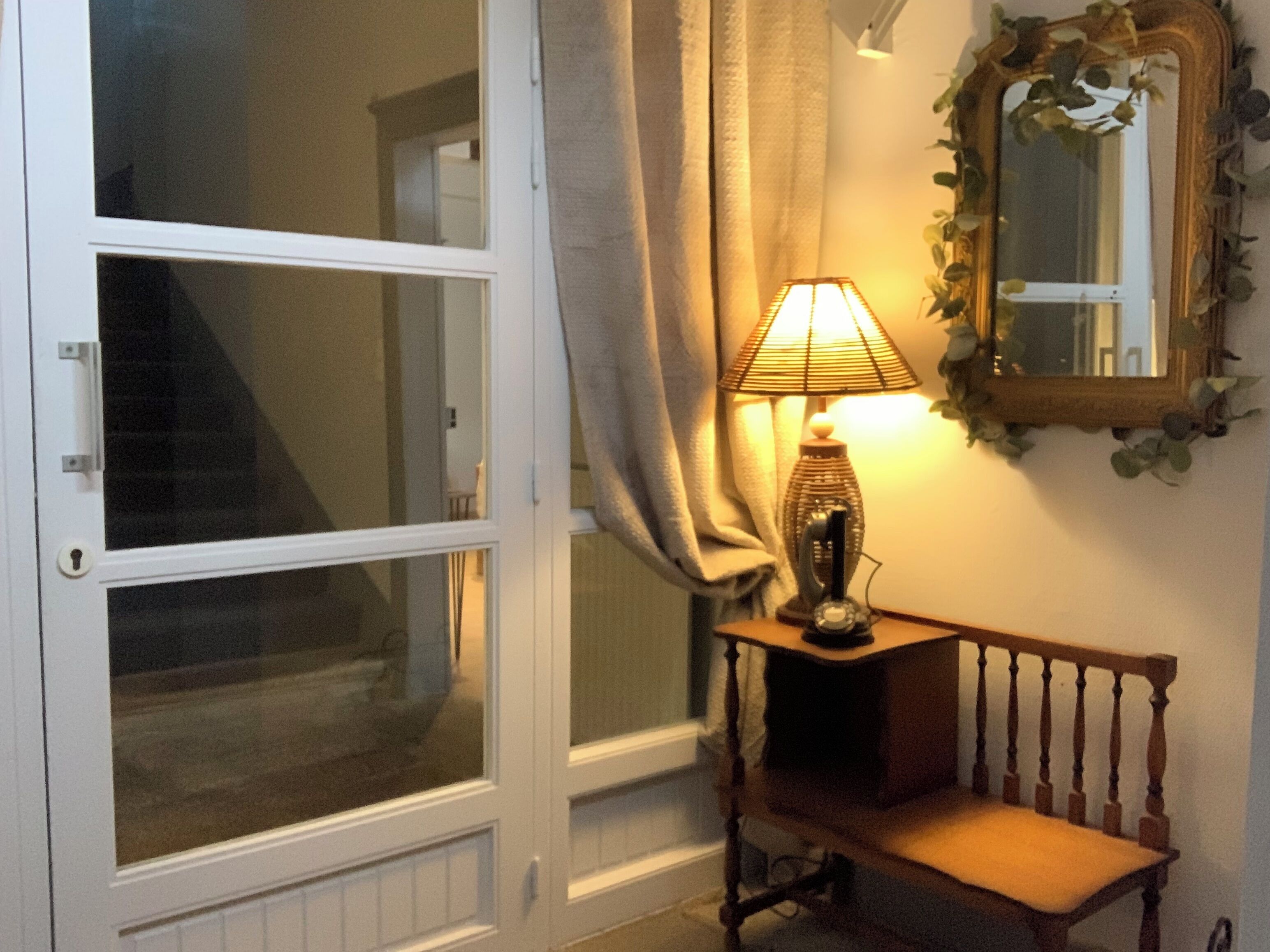 Une pièce avec une grande fenêtre, une lampe sur une petite table, un banc et un miroir au mur.