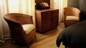 Quarto com duas cadeiras de vime, uma escrivaninha de madeira com livros e uma luminária.