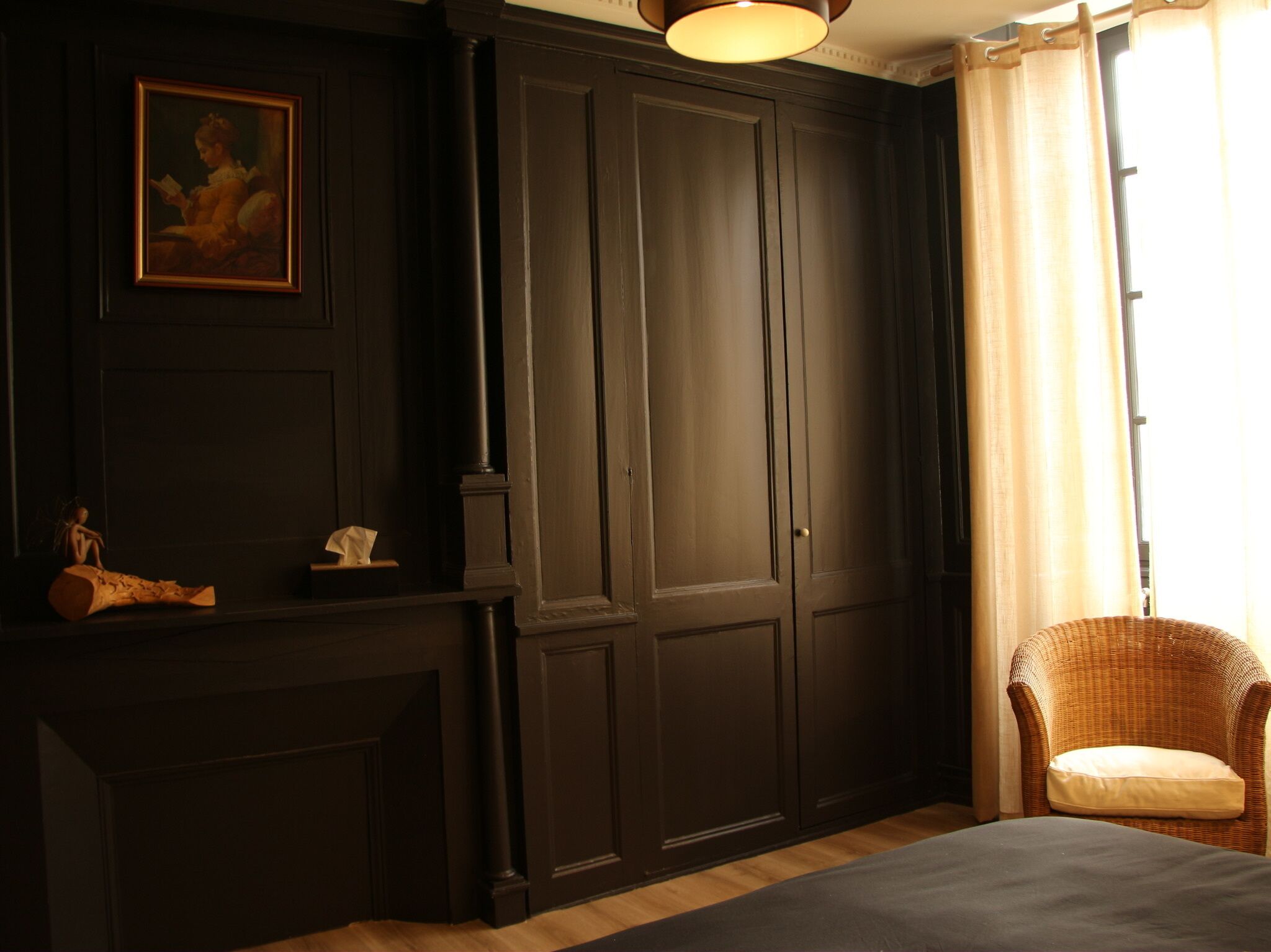 A room with dark wooden paneling, a fireplace, a wicker chair, and a window with curtains.
