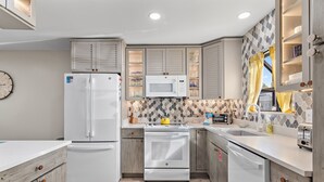 Una cocina moderna con electrodomésticos blancos, armarios de madera y salpicadero de azulejos.