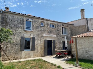 A stone building with a tiled roof, a small garden, and a table with chairs outside. - 3 stars: between land and sea, lovely house. (Saint-Just-Luzac)