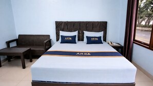 Een hotelkamer met een groot bed, twee kussens met 'ARBA'-logo, een donkerbruin hoofdeinde, een klein tafeltje en een stoel.
