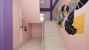 Een trap in een gebouw met roze muren en een brandblusser aan de linkerkant.