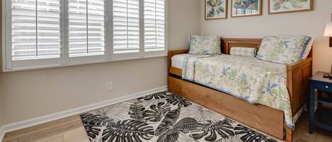 A bedroom with a bed, a ceiling fan, a window with blinds, and three wall-mounted paintings.