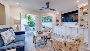 A living room with a sofa, armchair, and coffee table, a ceiling fan, and a TV mounted on the wall. - Angel Fish Cove | Updated Townhome Retreat Near Duval (Key West)