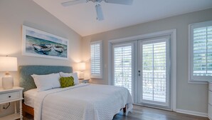 A bedroom with a large bed, a ceiling fan, a painting of boats, and a view through the door. - Angel Fish Cove | Updated Townhome Retreat Near Duval (Key West)
