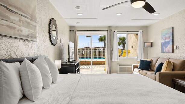 A bedroom with a large bed, a ceiling fan, a view of a pool, and a balcony with a railing. - The Ambassador - Unit C5 - Studio King - On Pool Deck (Panama City Beach)